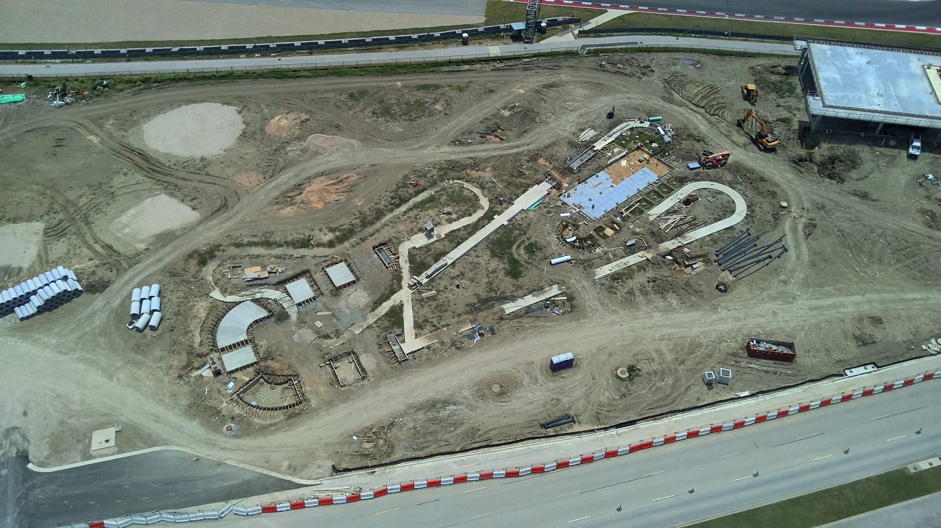 Aerial view of graded earthwork, staged culvert pipe and excavation equipment on a site under development